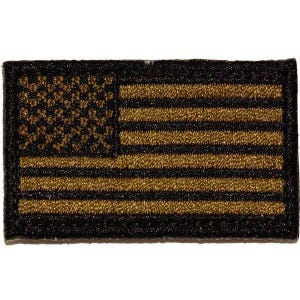 May include: A rectangular embroidered patch featuring a stylized American flag design. The patch displays a pattern of alternating black and metallic gold horizontal stripes, with a black field in the upper left corner containing gold stars.