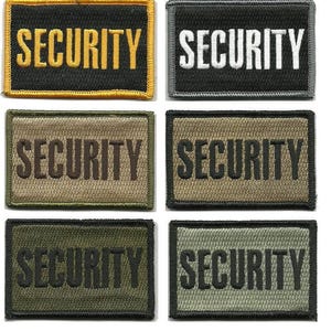 May include: A collection of six rectangular embroidered patches with the word "SECURITY" in bold capital letters. The patches vary in color, including black, gray, olive green, and tan, with the text in contrasting colors like yellow and white.