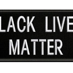May include: Black rectangular patch with the embroidered text "BLACK LIVES MATTER" in white. The patch has a black border and is likely made of fabric.