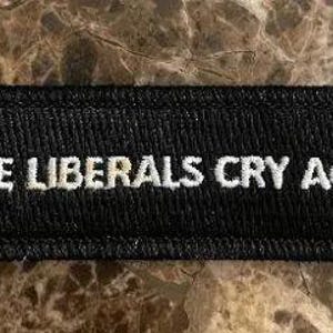 May include: Black rectangular patch with white embroidered text that reads "MAKE LIBERALS CRY AGAIN". The patch has a black border and is likely made of fabric.