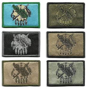 May include: Embroidered patches in various colors, including blue, green, black, and tan. Each patch features a central design with a circular emblem, crossed arrows, and a sprig of leaves. The patches are rectangular with a stitched border.