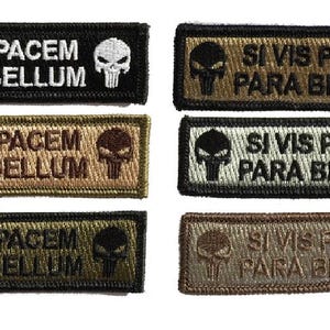 May include: Rectangular embroidered patches in various colors, including black, olive green, and tan. Each patch features the phrase "SI VIS PACEM PARA BELLUM" in white or tan, along with a skull graphic.