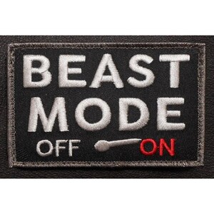 May include: A rectangular black embroidered patch featuring the white text BEAST MODE in large capital letters. Below the text is a toggle switch graphic with the word OFF in white and the word ON in red, indicating the switch is set to ON.