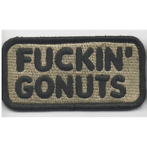 May include: A rectangular embroidered patch with a tan background and a thick black border. The text FUCKIN' GONUTS is stitched in bold black capital letters across the center of the patch. The design features a textured fabric appearance.