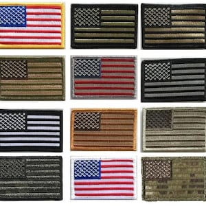May include: A collection of embroidered American flag patches in various colors and styles. The patches feature the stars and stripes design, with different color schemes including black, green, brown, and traditional red, white, and blue.