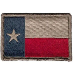 May include: A rectangular embroidered patch featuring the Texas state flag design. The patch has a vertical blue stripe on the left with a centered tan star, and horizontal tan and red stripes on the right, all bordered by a tan stitched edge.