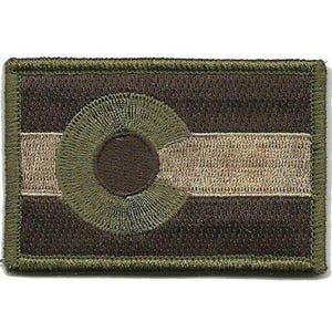 May include: A rectangular embroidered patch featuring a muted colour palette of dark brown, olive green, and tan. The design displays a stylised circular emblem centred over a horizontal band, with a thick, stitched olive green border edge.