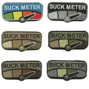 May include: Embroidered patches with the text "SUCK METER" above a gauge. The gauges have a needle and a color gradient, ranging from green to red. Patches come in various color schemes, including blue, black, brown, and green.