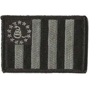 May include: A rectangular embroidered patch featuring a black and grey Gadsden flag design. The patch displays a coiled rattlesnake surrounded by thirteen stars in the upper left corner, with alternating black and grey vertical stripes throughout.