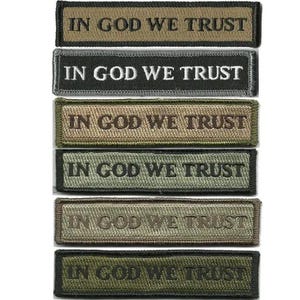 May include: Rectangular embroidered patches in various shades of green, brown, and black. Each patch features the text "IN GOD WE TRUST" in a contrasting color. The patches are likely designed for attachment to clothing or gear.