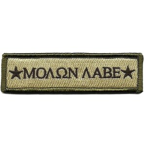 May include: A rectangular embroidered patch with a tan background and a dark olive green border. The text "ΜΟΛΩΝ ΛΑΒΕ" is stitched in dark brown thread across the center, flanked by a dark brown five-pointed star on both the left and right sides.
