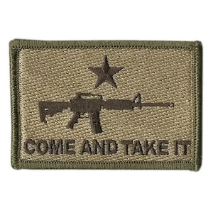 May include: A rectangular olive green embroidered patch featuring a dark brown rifle silhouette centered below a five-pointed star. The text "COME AND TAKE IT" is stitched in dark brown capital letters along the bottom edge of the patch.