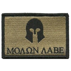 May include: A rectangular patch with a black embroidered border, a tan background, and a black Spartan helmet graphic centered above the Greek text "ΜΟΛΩΝ ΛΑΒΕ" in black lettering. The design features a clean, high-contrast aesthetic.