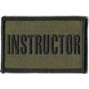 May include: A rectangular embroidered patch with an olive green background and a black border. The word INSTRUCTOR is stitched in bold, black, capital letters across the center of the patch, featuring a textured thread finish throughout.