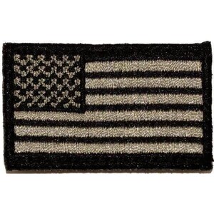 May include: A rectangular embroidered patch featuring the United States flag in a monochromatic black and grey color scheme. The design consists of a dark field with embroidered stars and alternating horizontal stripes in a muted grey tone.