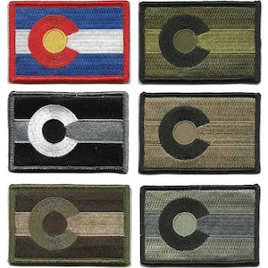 May include: A collection of rectangular patches featuring the Colorado state flag and variations. The Colorado flag patch has a red C, a yellow circle, and blue and white stripes. Other patches have a C design in various colors like black, green, and brown.