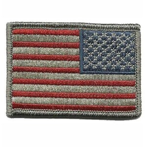 Op de afbeelding: Een rechthoekige geborduurde patch met de vlag van de Verenigde Staten in een gedempt kleurenpalet. Het ontwerp bestaat uit horizontale strepen in afwisselende tinten donkerrood en grijs, met een donkerblauw kanton met kleine grijze sterren.