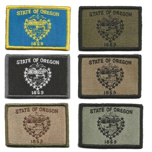 May include: Rectangular embroidered patches featuring the Oregon state seal and the text "STATE OF OREGON" and "1859". The patches come in various colors, including blue, green, black, and tan, with the seal in contrasting colors.