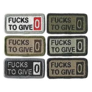 May include: Six embroidered patches with the text "FUCKS TO GIVE 0" in various colors, including gray, olive green, and black. The patches are rectangular with a stitched border.