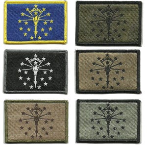 May include: A collection of six embroidered patches featuring the Indiana state flag design. The patches showcase the state's torch and star emblem in various color schemes, including blue, black, and olive green. Each patch is rectangular with a stitched border.