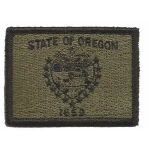 Peut inclure: Un écusson rectangulaire brodé vert olive portant le texte STATE OF OREGON en haut et 1859 en bas. Le centre présente un emblème brodé détaillé du sceau de l'État de l'Oregon, le tout bordé par un épais contour noir brodé.