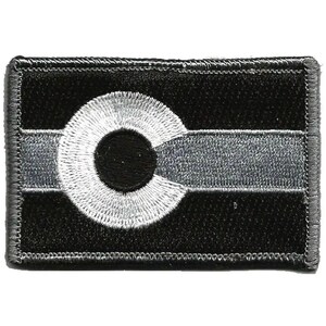May include: A rectangular embroidered patch featuring a monochromatic design of the Colorado state flag. The patch displays a black background with a horizontal grey stripe across the centre and a large white letter C with a black centre circle.