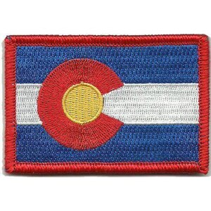 May include: A rectangular embroidered patch featuring the Colorado state flag design. The patch has a blue, white, and blue horizontal striped background with a large red letter C and a yellow circle in the centre, finished with a red border.