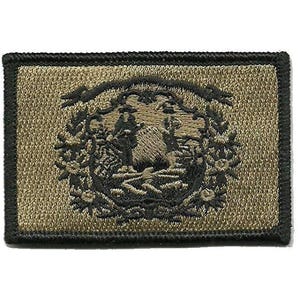 May include: A rectangular embroidered patch featuring a tan background with a black stitched border. The center displays a detailed black thread design of a circular emblem containing two figures standing in a landscape with floral motifs.