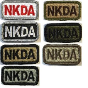 May include: A collection of rectangular embroidered patches with the letters "NKDA" in various color combinations. Patches include red on white, black on silver, olive green on black, and tan on brown.