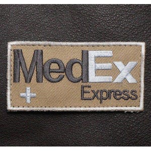 May include: A rectangular embroidered patch with a tan background and a white border. The text MedEx is stitched in dark gray and white, with the word Express in dark gray below it. A small white cross symbol is positioned to the left of the text.