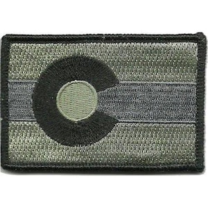 May include: A rectangular embroidered patch featuring a muted olive green and dark grey colour scheme. The design displays a stylised letter C in black, surrounding a central olive green circle, mimicking the Colorado state flag design.