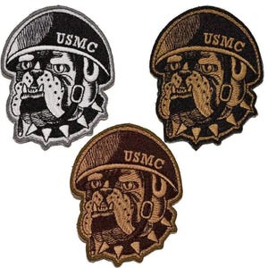 May include: Three embroidered patches featuring a bulldog wearing a helmet with the text "USMC". The patches are in black and white, black and gold, and brown and tan. The bulldog has a fierce expression.