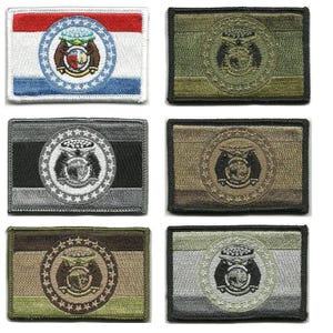 May include: Embroidered patches in various colors, including green, gray, and tan. Each patch features a circular emblem with a detailed design, surrounded by stars. One patch displays a flag design with red, white, and blue stripes.