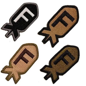 May include: Four embroidered patches in the shape of a bomb, each with a large letter "F". The patches are in black, tan, and brown colors, with the "F" in contrasting colors. The patches have a detailed, textured appearance.
