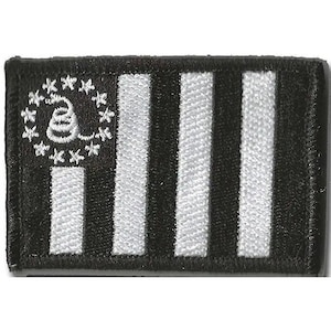 May include: A rectangular embroidered patch featuring a black and white design. The left side displays a coiled snake surrounded by a circle of thirteen stars, while the right side consists of alternating black and white vertical stripes.