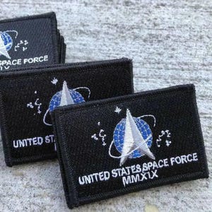 May include: Black embroidered patches featuring the United States Space Force logo. The patches display a white and blue emblem with the text "UNITED STATES SPACE FORCE" and "MMXIX". The patches are rectangular.