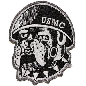 May include: An embroidered patch featuring a black and white illustration of a bulldog wearing a military helmet with the text USMC printed on the front. The bulldog has a spiked collar and a determined expression, rendered in high-contrast thread.