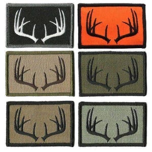 May include: A collection of six rectangular patches featuring embroidered deer antlers. The patches have various background colors, including black, orange, tan, and green. The antler colors contrast with the backgrounds, offering a variety of options.
