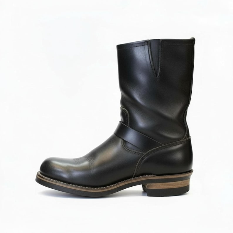 May include: Black leather boot with a rounded toe and a mid-calf shaft. The boot features a strap across the ankle and a stacked heel. The sole is brown with a light-coloured stitch.
