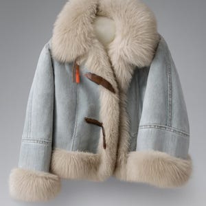 May include: Light blue denim jacket with a cream-colored fur collar, cuffs, and lining. The jacket features brown toggle closures and a small orange tag. A stylish winter coat.