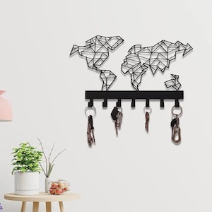 May include: A black metal key holder in the shape of a world map, mounted on a white wall. The key holder has six hooks with keys hanging from them. The map design is geometric, with the continents outlined in black.