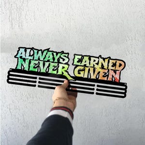 May include: Black metal medal display with the text "ALWAYS EARNED NEVER GIVEN" in a colorful gradient. The display has three horizontal bars for hanging medals.