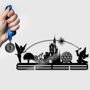 May include: Black metal medal display featuring a silhouette of a castle, a fairy, and a wizard. The display has three horizontal bars for hanging medals. A blue ribbon holds a silver medal with the number 1.