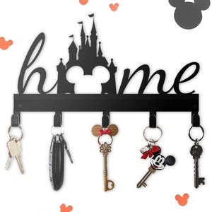 May include: Black metal key holder with the word "home" and a castle silhouette. Features five hooks with keys and keychains, including a Mickey Mouse design. Orange Mickey Mouse head and heart-shaped decorations.