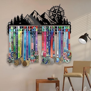 May include: Black metal medal display rack with a mountain and compass design. The rack holds numerous colourful medals with ribbons. The medals are of various sizes and shapes, some displaying text and graphics.
