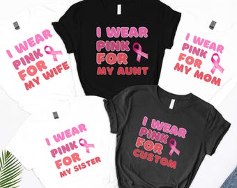 May include: Five t-shirts, in black and white, with the text "I WEAR PINK FOR" followed by "MY WIFE", "MY AUNT", "MY MOM", "MY SISTER", and "CUSTOM". Each shirt has a pink ribbon graphic, symbolizing breast cancer awareness.
