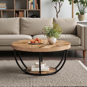 May include: A circular coffee table with a wooden top featuring a herringbone design and a black metal frame. The table has a lower shelf and is positioned in front of a beige sofa. A vase of flowers and a plate of apples are on the table.