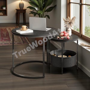 May include: A set of two round side tables with dark wood surfaces and black metal frames. The larger table has a laptop and a cup. The smaller table has a basket underneath and a bowl of fruit on top.