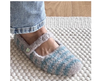 May include: A Mary Jane style slipper crafted from fuzzy, light purple yarn with horizontal stripes in a soft blue hue. The slipper features a single strap across the top secured by a small, round, iridescent button on the side of the footwear.
