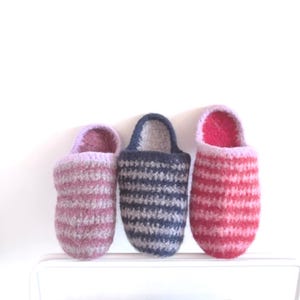 Peut inclure: Trois pantoufles tricotées à rayures roses, bleues et rouges. Les pantoufles ont un aspect doux et confortable. Elles sont conçues pour un usage intérieur et sont présentées sur une surface blanche.